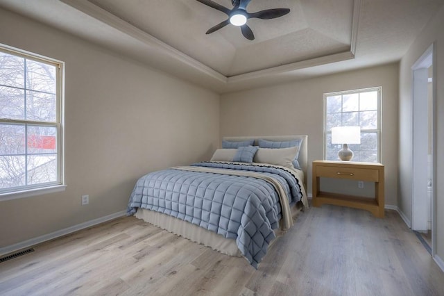 bedroom with light wood-type flooring, multiple windows, visible vents, and a raised ceiling