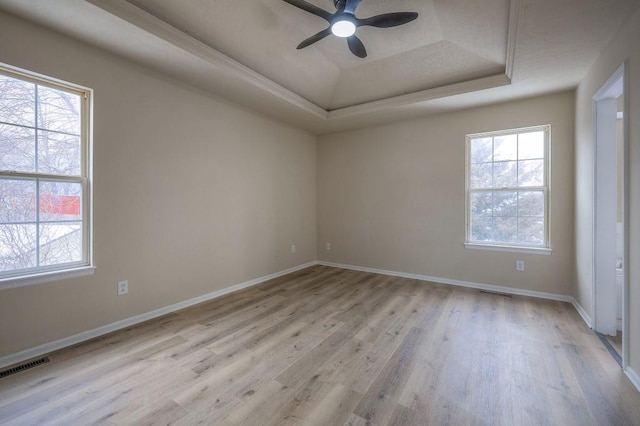 unfurnished room featuring a tray ceiling, plenty of natural light, light wood-style flooring, and visible vents