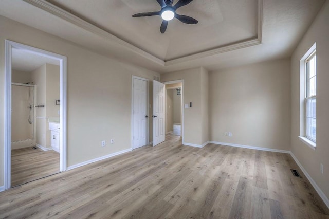 unfurnished bedroom featuring a raised ceiling, multiple windows, and light wood finished floors