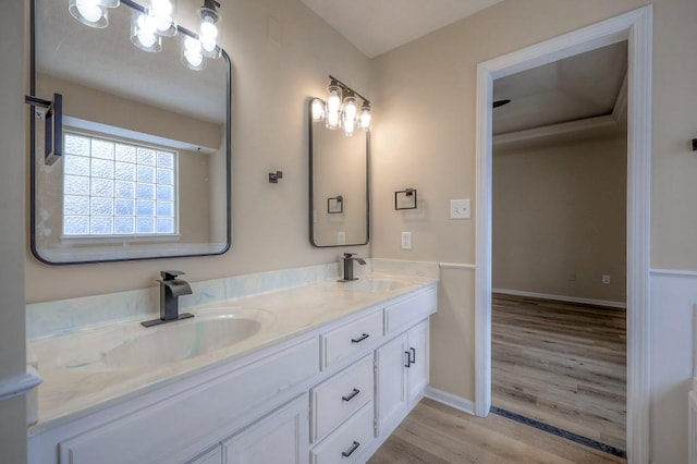 bathroom with double vanity, baseboards, a sink, and wood finished floors