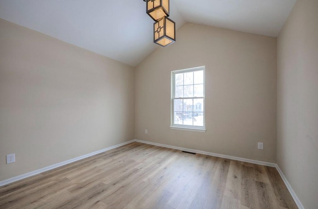 spare room featuring light wood-type flooring, visible vents, lofted ceiling, and baseboards