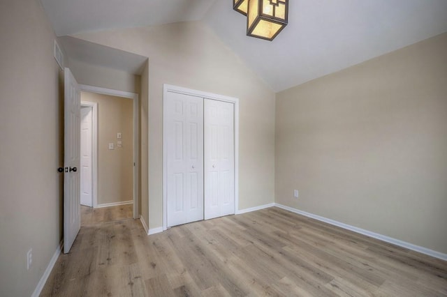 unfurnished bedroom with light wood-style floors, lofted ceiling, a closet, and baseboards