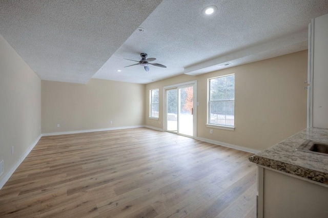 unfurnished living room with light wood-style floors, ceiling fan, baseboards, and a textured ceiling