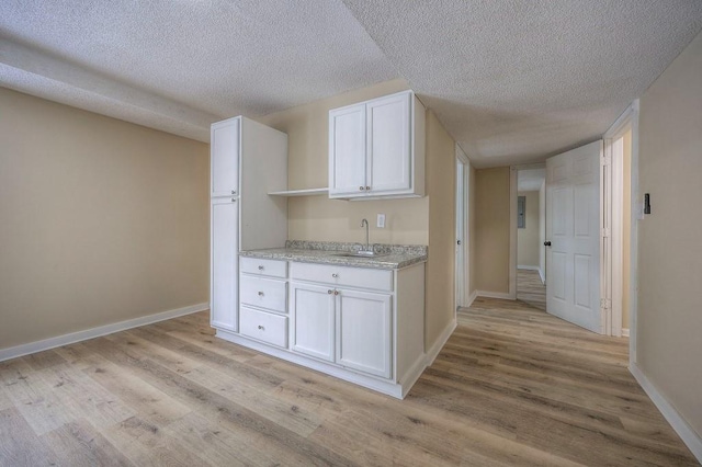 kitchen with light wood-style floors, white cabinets, a sink, a textured ceiling, and baseboards