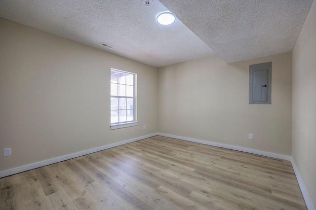 empty room featuring a textured ceiling, visible vents, baseboards, light wood-style floors, and electric panel