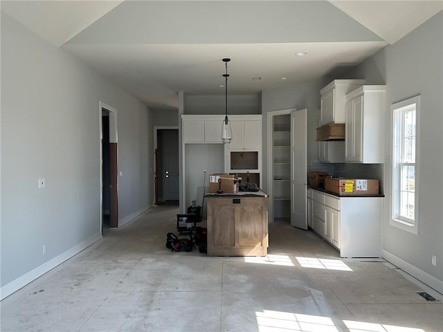 kitchen featuring dark countertops, a center island, baseboards, decorative light fixtures, and white cabinets