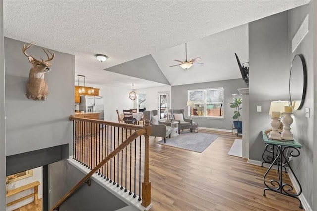 hall featuring light wood-style floors, a textured ceiling, and an upstairs landing