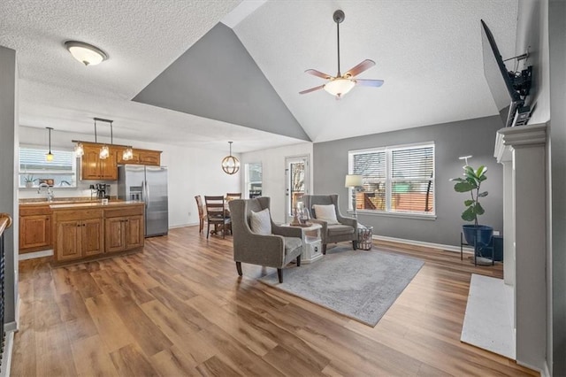 living area with lofted ceiling, light wood-style flooring, a textured ceiling, and ceiling fan with notable chandelier