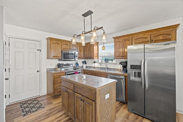 kitchen featuring a center island, decorative light fixtures, stainless steel appliances, light countertops, and a sink