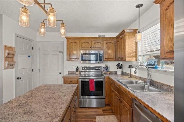 kitchen with stainless steel appliances, hanging light fixtures, brown cabinetry, and a sink