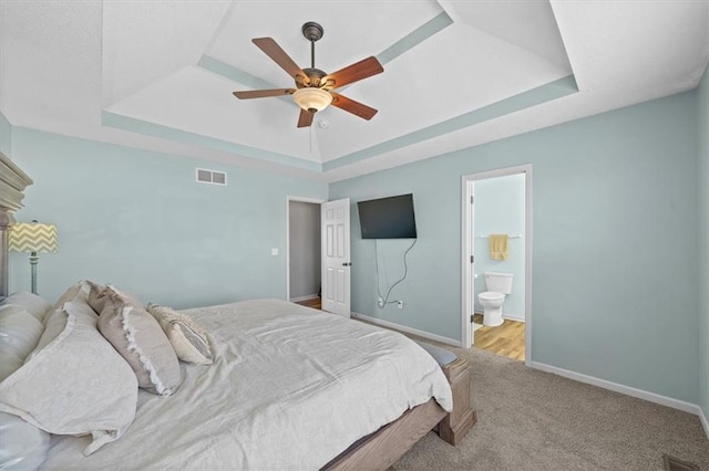 bedroom featuring visible vents, connected bathroom, a tray ceiling, and baseboards