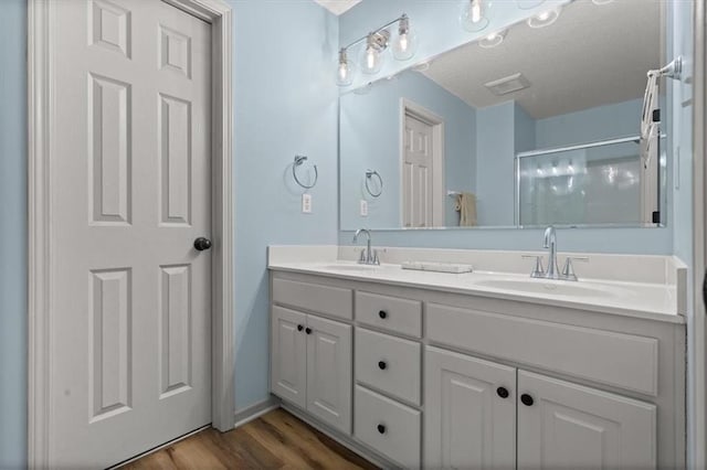 full bath featuring double vanity, wood finished floors, a sink, and a shower stall