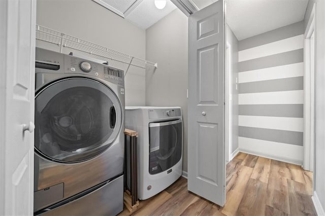 laundry area featuring laundry area, baseboards, light wood-style flooring, and washing machine and clothes dryer