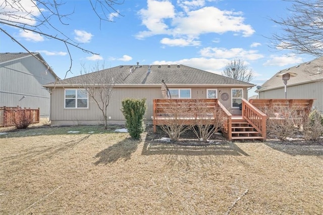 rear view of property featuring a deck, a yard, a shingled roof, and fence