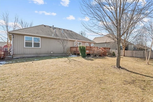 rear view of house featuring a deck, roof with shingles, a lawn, and fence