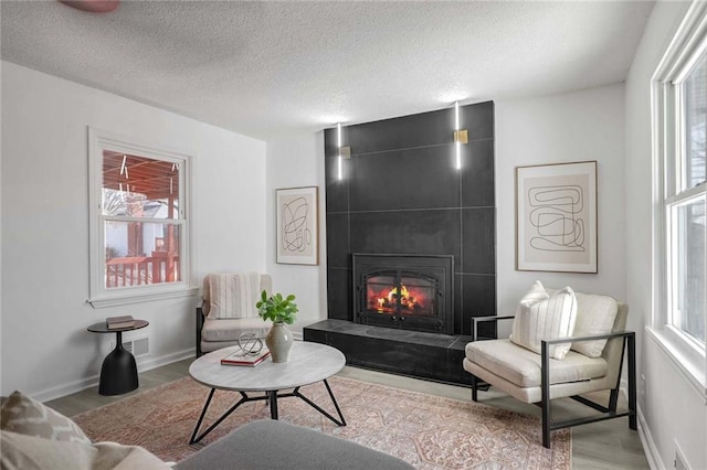 living area featuring a large fireplace, a textured ceiling, light wood-style flooring, and baseboards