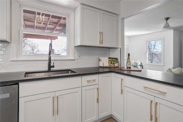 kitchen with tasteful backsplash, dark countertops, stainless steel dishwasher, white cabinets, and a sink