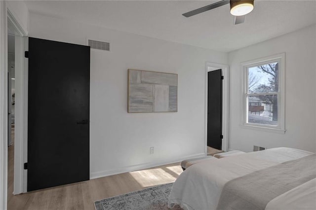 bedroom with light wood finished floors, ceiling fan, visible vents, and baseboards