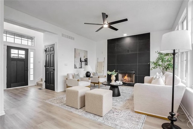 living room featuring light wood finished floors, a fireplace, visible vents, and a ceiling fan