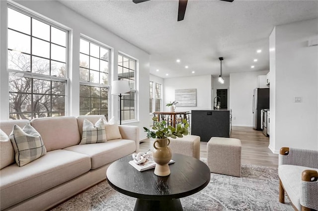 living area featuring a textured ceiling, recessed lighting, wood finished floors, a ceiling fan, and baseboards