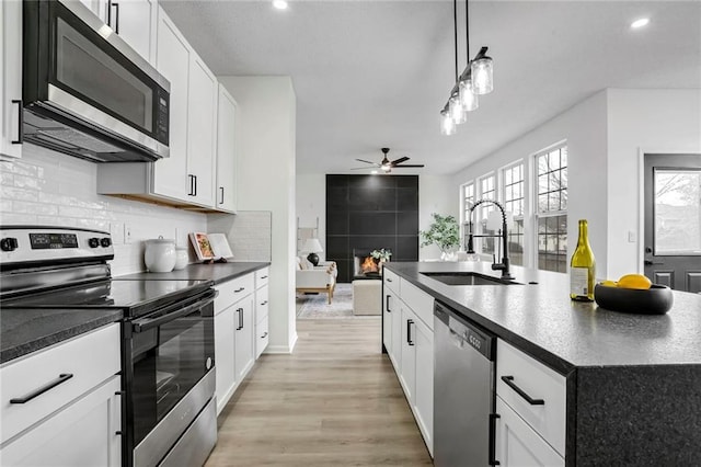 kitchen with dark countertops, hanging light fixtures, appliances with stainless steel finishes, a sink, and an island with sink