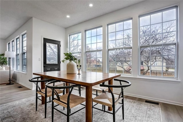 dining area featuring a textured ceiling, light wood-style flooring, recessed lighting, visible vents, and baseboards