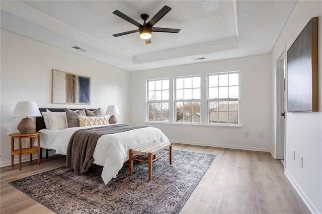 bedroom featuring light wood finished floors, a raised ceiling, and visible vents