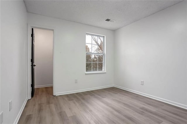 empty room with light wood-type flooring, visible vents, a textured ceiling, and baseboards