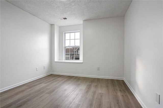 empty room featuring baseboards, a textured ceiling, visible vents, and wood finished floors