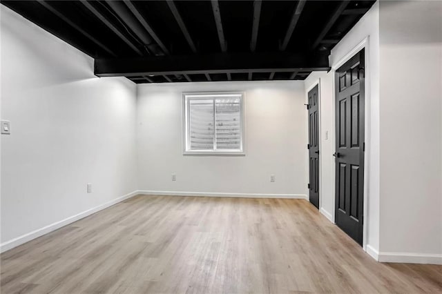 empty room featuring beamed ceiling, light wood-style flooring, and baseboards