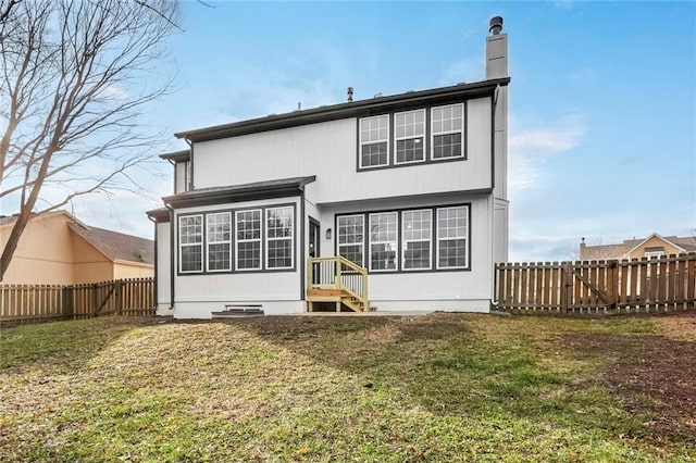 back of property with entry steps, a fenced backyard, a chimney, and a lawn