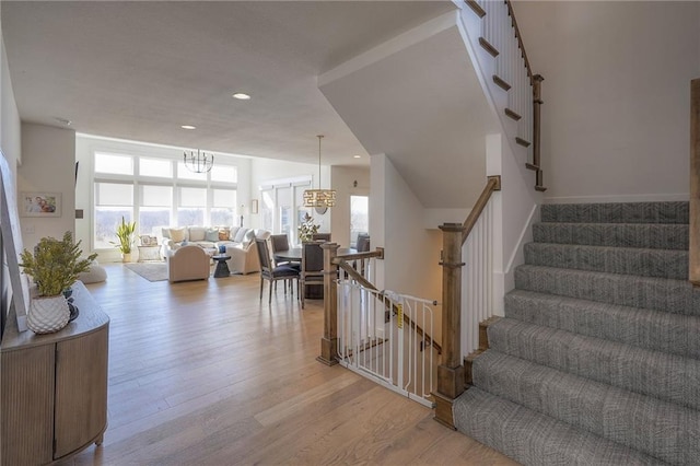 stairway with a healthy amount of sunlight, recessed lighting, a notable chandelier, and wood finished floors