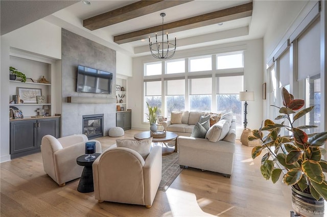 living room with a tile fireplace, an inviting chandelier, a high ceiling, light wood-style floors, and beam ceiling