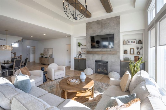 living room with built in features, a notable chandelier, a tiled fireplace, wood finished floors, and beamed ceiling