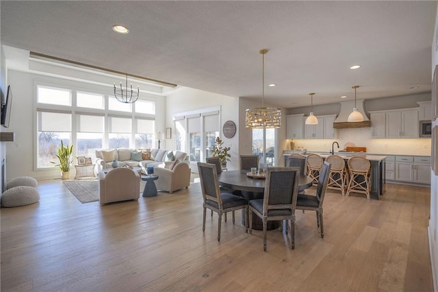 dining area with light wood-type flooring, a notable chandelier, a textured ceiling, and recessed lighting