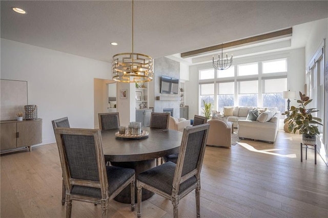 dining space featuring recessed lighting, a fireplace, light wood-style flooring, and an inviting chandelier