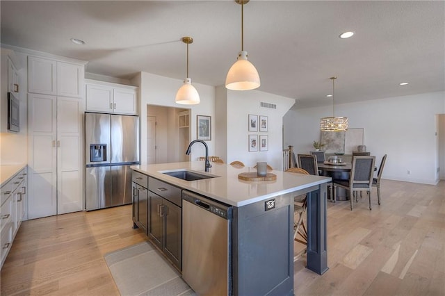 kitchen featuring appliances with stainless steel finishes, light countertops, a sink, and light wood-style flooring