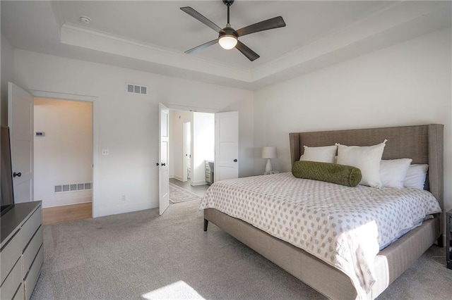 bedroom with light colored carpet, a tray ceiling, and visible vents