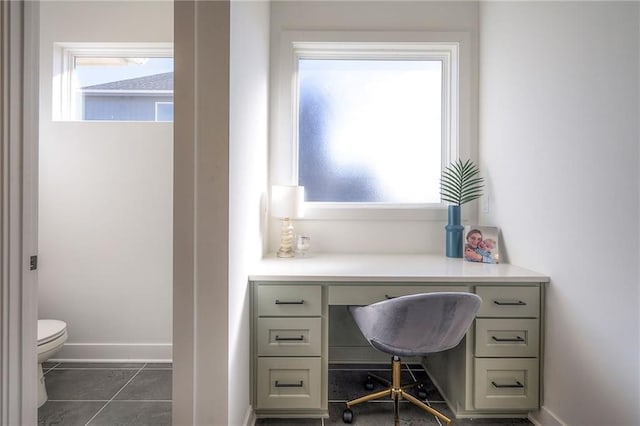 home office with dark tile patterned floors, baseboards, and built in desk