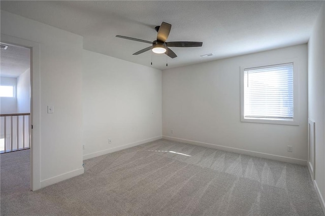 spare room with a ceiling fan, light colored carpet, visible vents, and baseboards