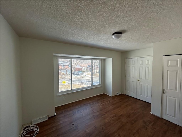 unfurnished bedroom featuring dark wood-style floors, a textured ceiling, a closet, and visible vents