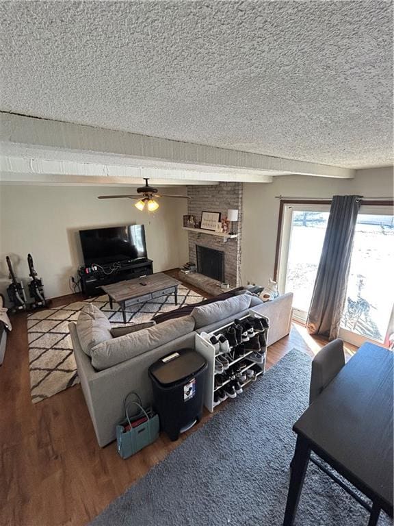 living area with a textured ceiling, ceiling fan, a fireplace, and wood finished floors