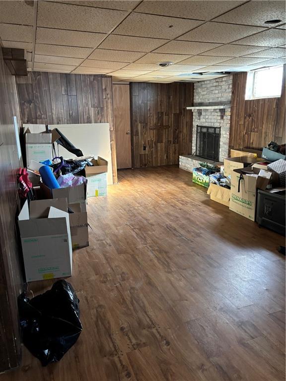 basement with a paneled ceiling, a fireplace, wood walls, and wood finished floors