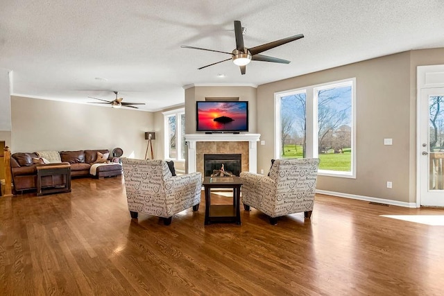 living area with dark wood-style floors, ceiling fan, a textured ceiling, and a tiled fireplace