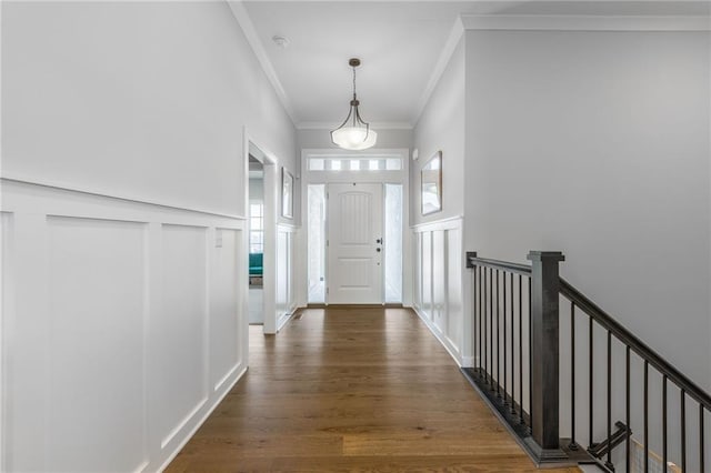 interior space with a wainscoted wall, crown molding, a decorative wall, and dark wood-style flooring