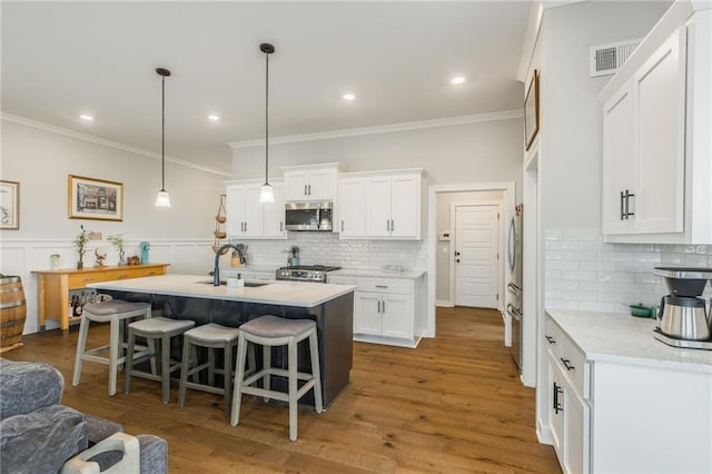 kitchen with visible vents, appliances with stainless steel finishes, white cabinetry, a sink, and a kitchen bar