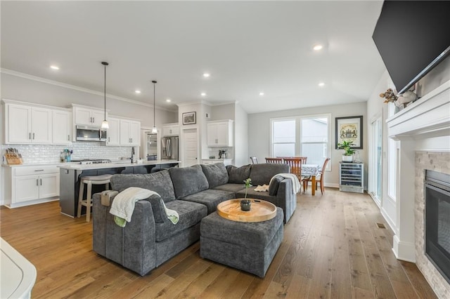 living room featuring wine cooler, recessed lighting, ornamental molding, a glass covered fireplace, and hardwood / wood-style flooring