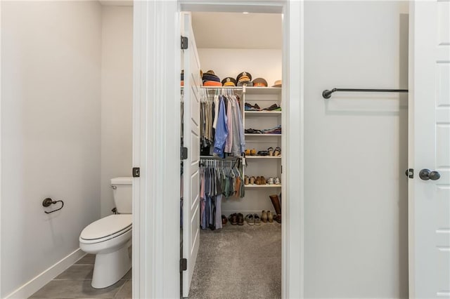 bathroom with a spacious closet, toilet, and baseboards