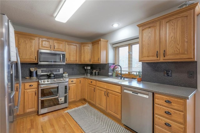 kitchen with appliances with stainless steel finishes, a sink, light wood-style flooring, and decorative backsplash