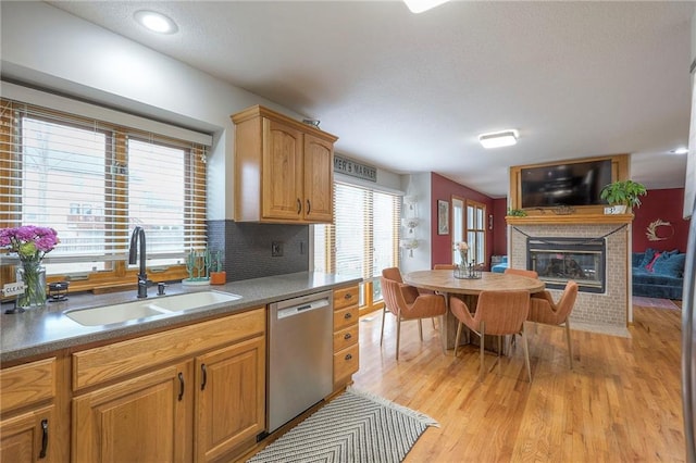 kitchen with backsplash, light wood-style floors, a brick fireplace, a sink, and dishwasher